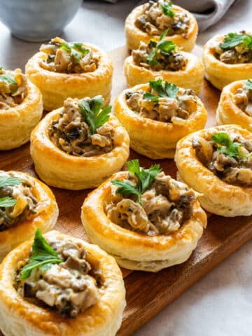 Chicken and mushroom vol-au-vents with a creamy filling, topped with fresh parsley and arranged on a wooden serving board.