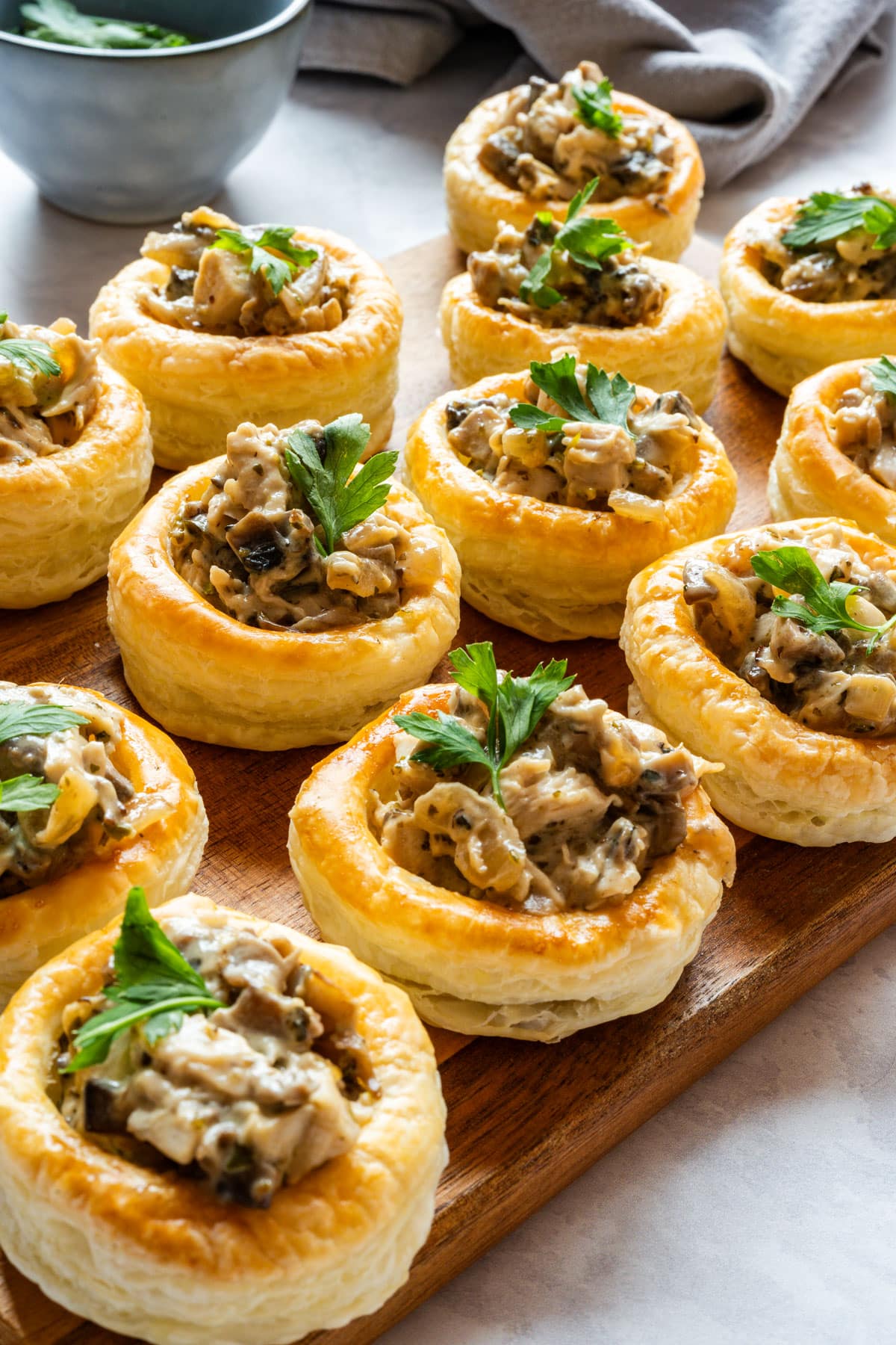 Chicken and mushroom vol-au-vents with a creamy filling, topped with fresh parsley and arranged on a wooden serving board.