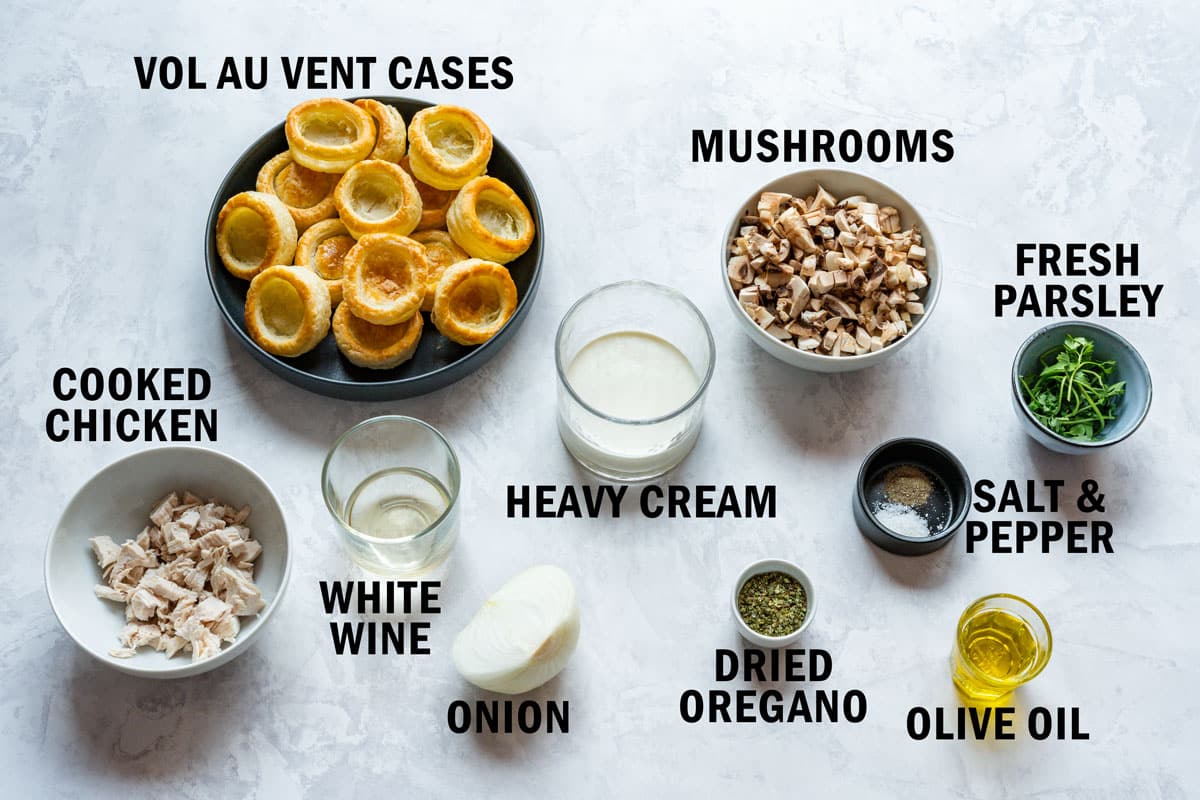 Ingredients for the filling next to baked vol-au-vent cases: cooked chicken, diced mushrooms, heavy cream, white wine, onion, dried oregano, olive oil, salt, pepper and fresh parsley.