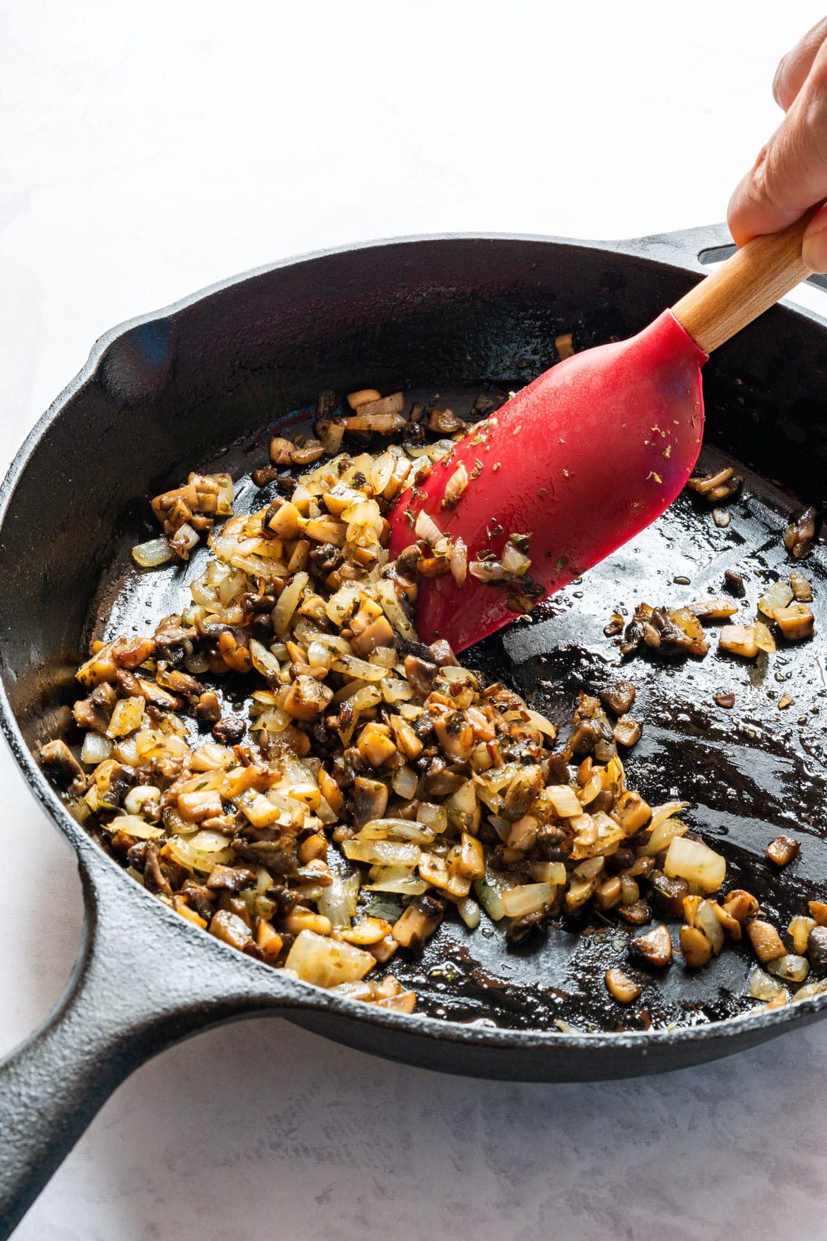 Stirring sautéed onion and diced mushrooms with dried oregano in a cast-iron skillet.