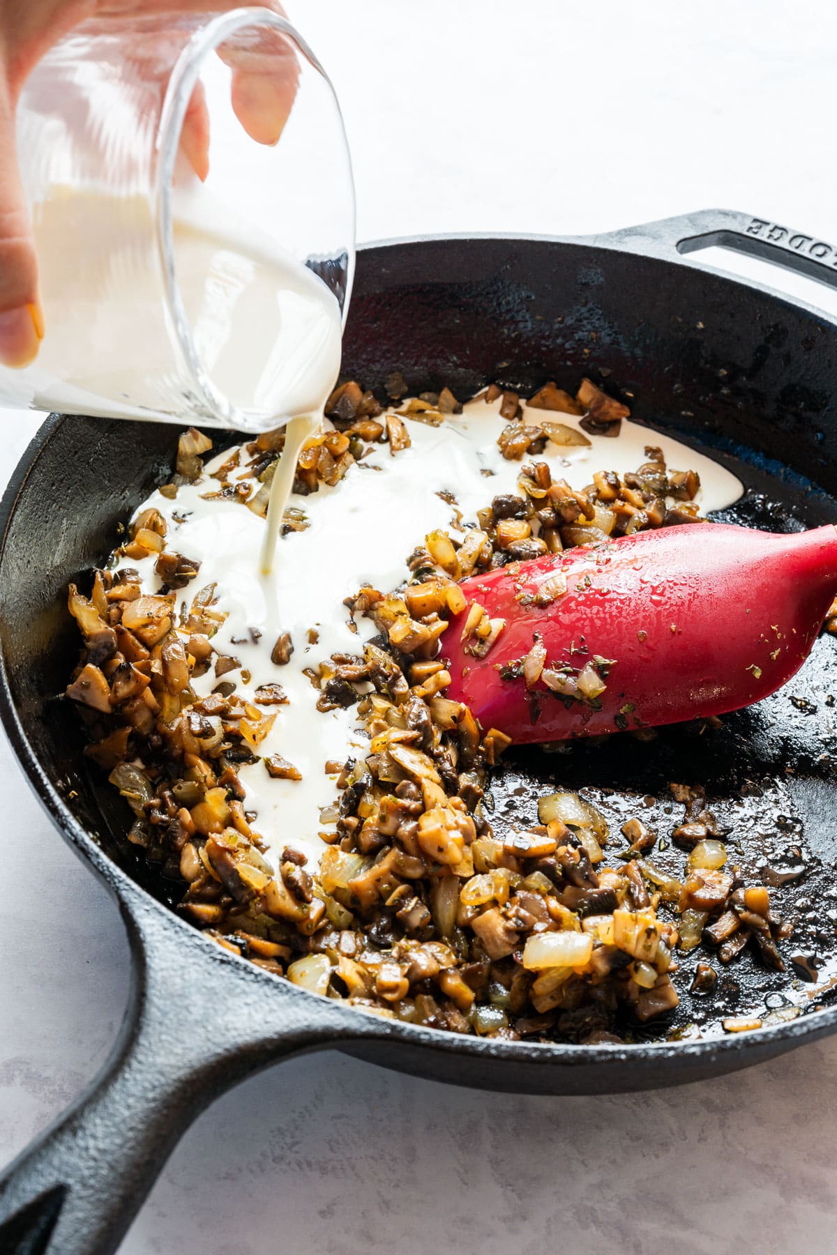 Pouring heavy cream over the sautéed mushrooms and onion in the skillet.