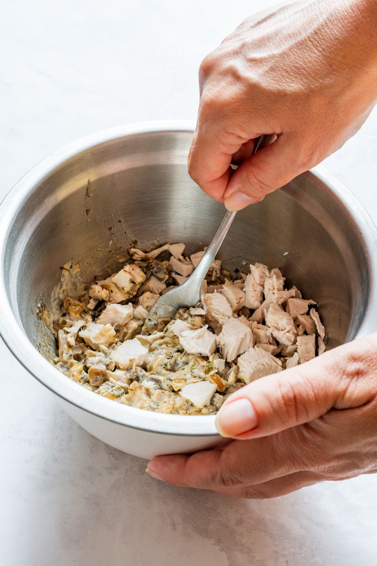 Mixing diced cooked chicken into the creamy mushroom sauce with a fork in a metal bowl.