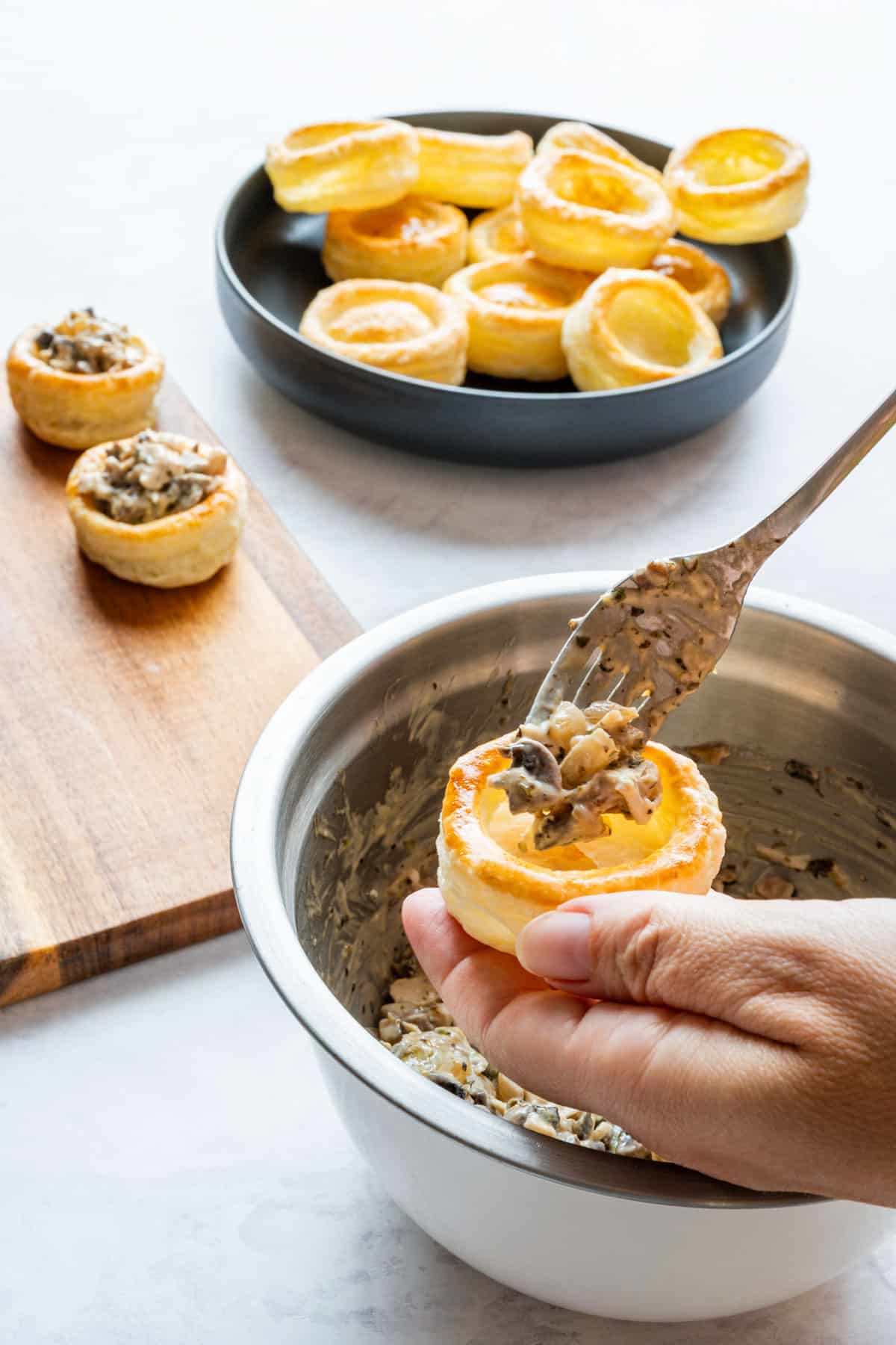 Adding the chicken and mushroom filling to an empty puff pastry case with a fork.