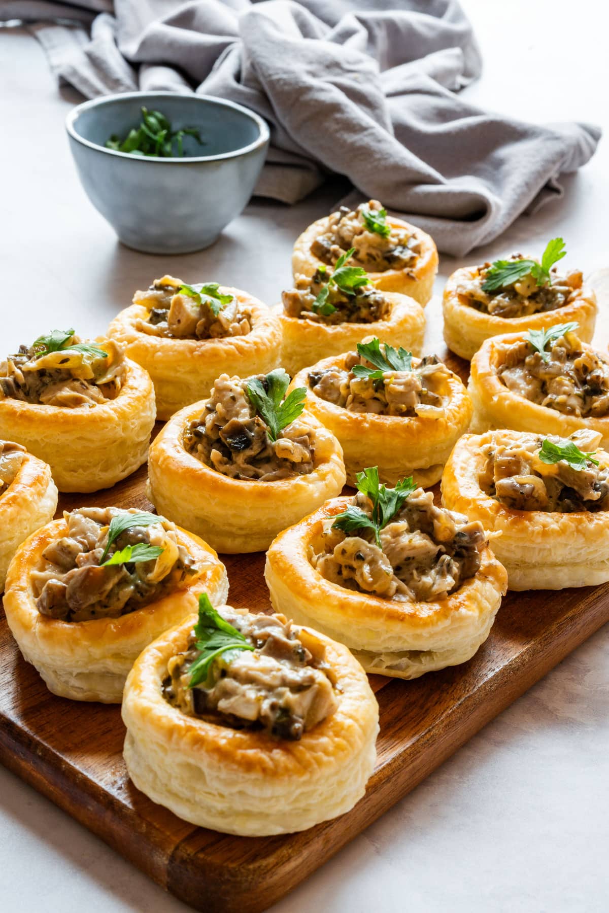 Puff pastry cases filled with creamy chicken and mushrooms and topped with fresh parsley on a wooden board.