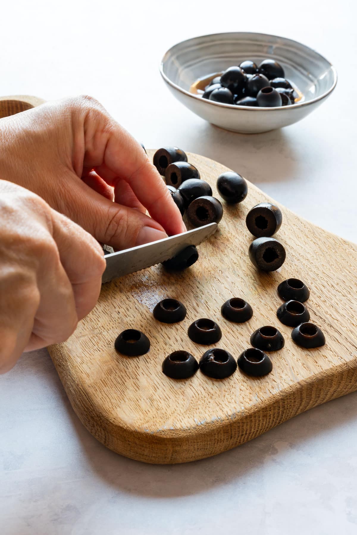 Cutting rings from the pitted black olives on a wooden board.