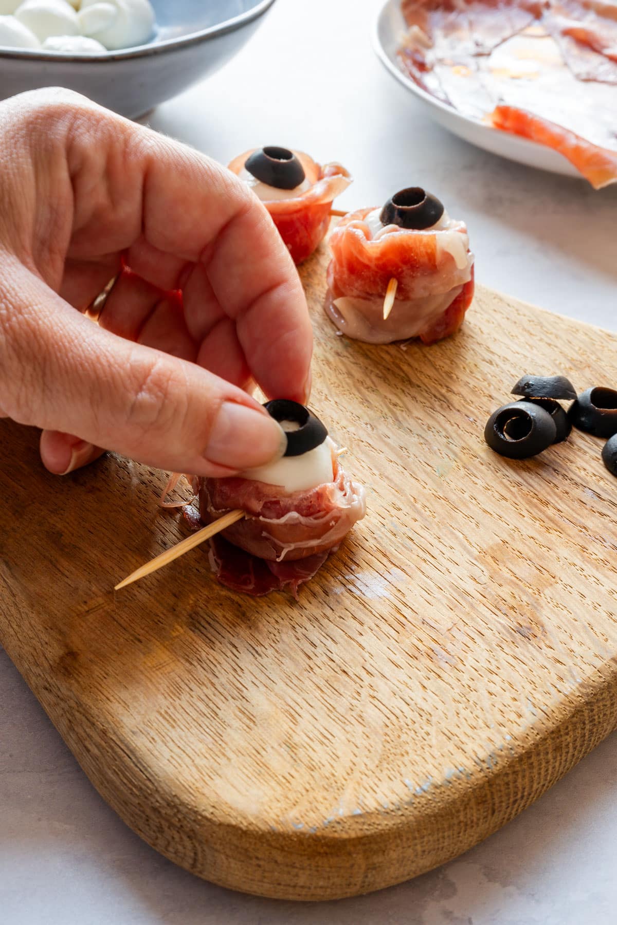 Adding a black olive ring to a prosciutto-wrapped mozzarella ball to make the pupil.