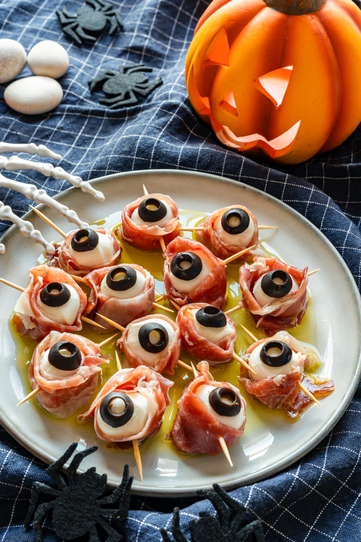 Prosciutto-wrapped mozzarella balls with black olive pupils on a plate, with Halloween decorations around them.