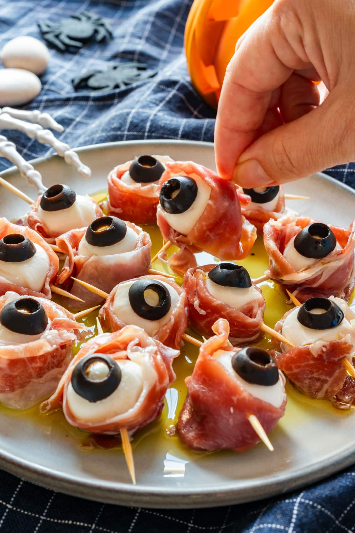 Hand picking up a mozzarella eyeball from a plate with a thin layer of olive oil.