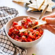 A tortilla chip piled with watermelon salsa above the bowl. This fresh summer salsa is made with red onion, cilantro, mint and lemon, with no jalapeƱos or hot peppers, so it stays mild enough for the whole family.