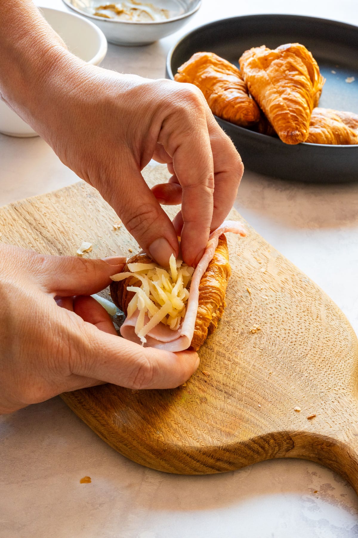 Tucking a slice of ham and shredded Gruyère into a cut croissant.