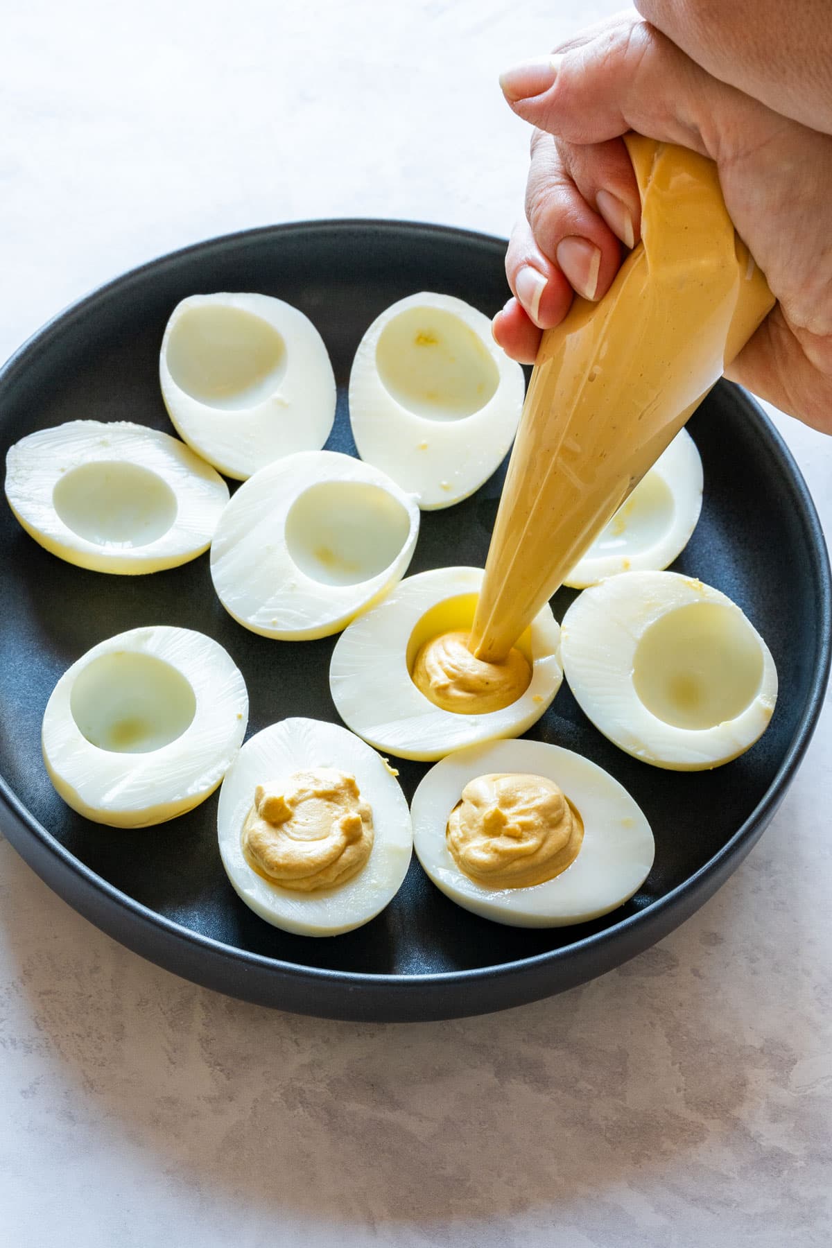 Piping the yolk filling into egg white halves on a black plate.