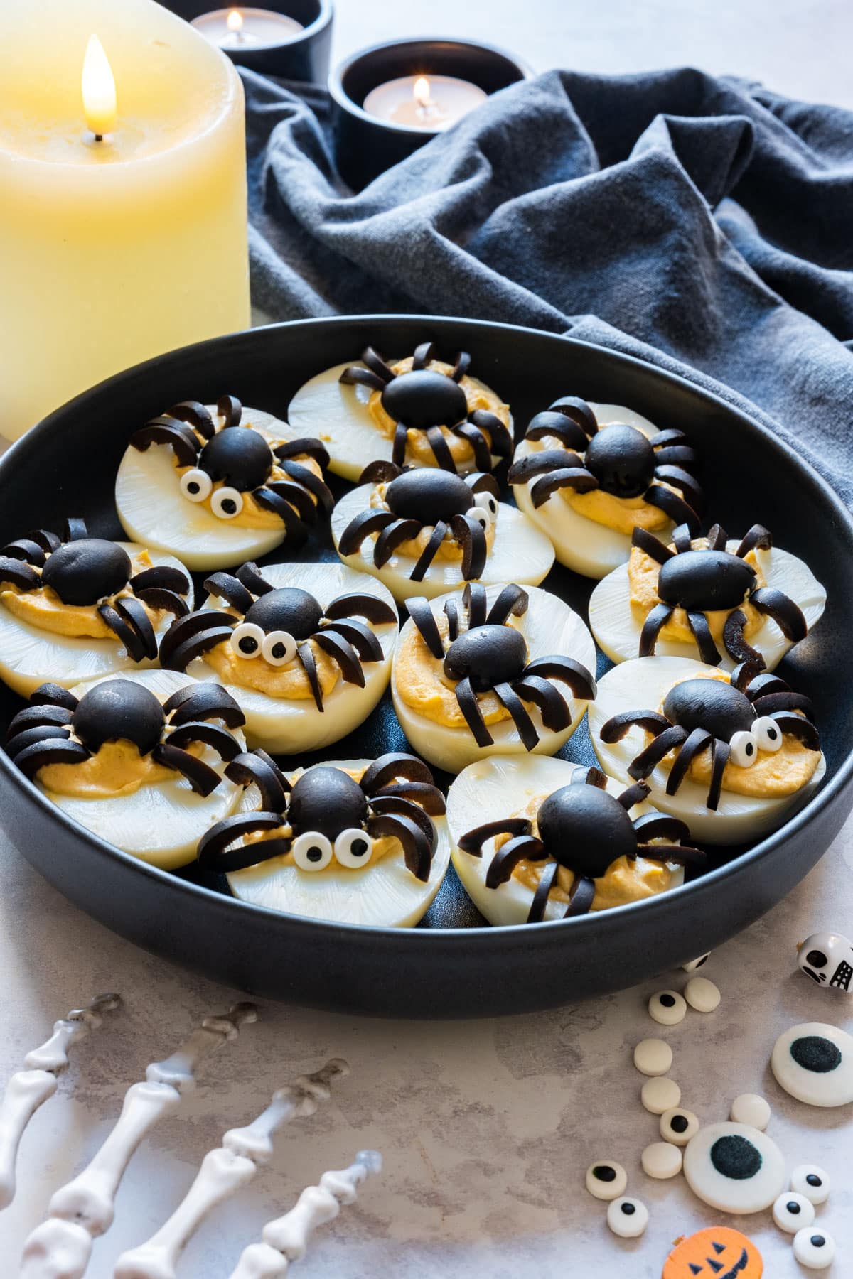 Halloween deviled eggs topped with olive spiders, with a pillar candle and tealights in the background.